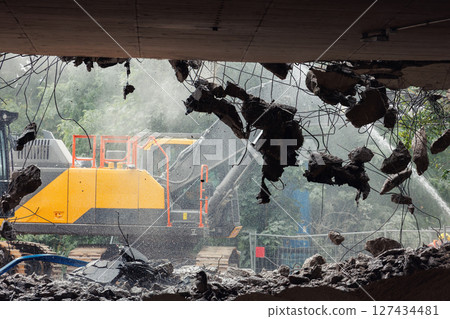 Close-up view of crumbling bridge structure demolition in Magdeburg Damaschkeplatz exposed steel rebar falling concrete chunks. Rubble piles and demolition machinery emphasize destruction progress Close-up view of crumbling bridge structure demolition in Magdeburg Damaschkeplatz exposed steel rebar falling concrete chunks. Rubble piles and demolition machinery emphasize destruction progress 127434481