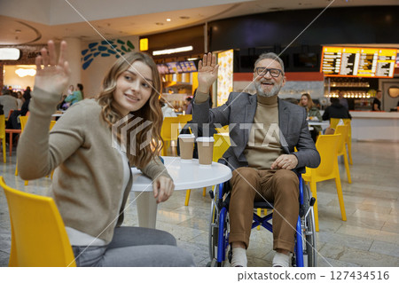 Mature man in wheelchair sharing moment in a shopping centre with lady assistant Mature man in wheelchair sharing moment in a shopping centre with lady assistant 127434516