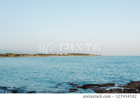 Rocky sea coast overlooking calm blue sea and clear sky. Natural landscape with limestone formations and rough rocky surface at water's edge. Summer sunny scene without people. 127434582