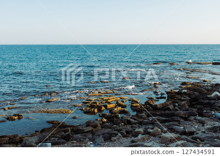 Rocky sea coast overlooking calm blue sea and clear sky. Natural landscape with limestone formations and rough rocky surface at water's edge. Summer sunny scene without people. Rocky sea coast overlooking calm blue sea and clear sky. Natural landscape with limestone formations and rough rocky surface at water's edge. Summer sunny scene without people. 127434591