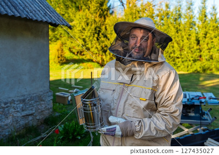 Beekeeper in Protective Suit Holding Smoker for Bee Control in Outdoor Setting 127435027