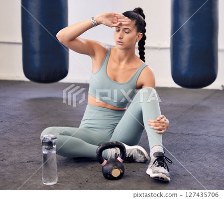 Fitness, tired and woman with burnout or headache, break and relax after workout in gym, water bottle and kettlebell for weightlifting. Bodybuilder, exercise and exhausted from sports and cardio. 127435706