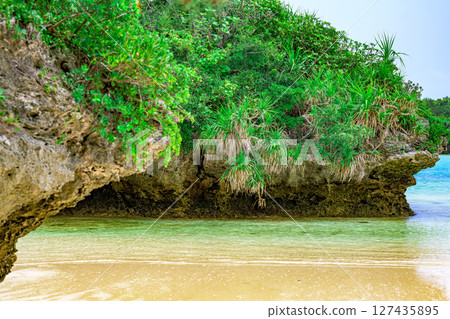 A small green rock formation floating in the clear waters of Ishigaki Island, blue sky and emerald green sea 127435895