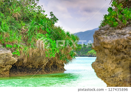 A small green rock formation floating in the clear waters of Ishigaki Island, blue sky and emerald green sea 127435896