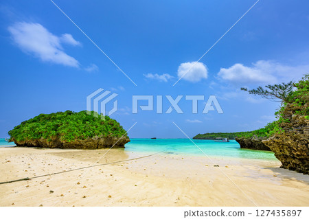 A small green rock formation floating in the clear waters of Ishigaki Island, blue sky and emerald green sea 127435897