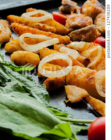 Oven pan with sliced baked potatoes, fish steaks and vegetables with onion on the table. Homemade healthy dinner with potatoes and seafood. 127436289