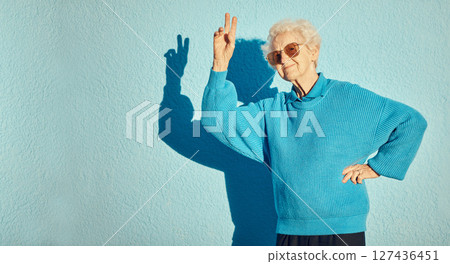 City, fashion and senior woman with peace sign on blue background wall enjoy freedom, weekend and retirement. Energy, hand sign and happy elderly female with cool, modern and trendy clothes in town 127436451