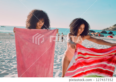 Woman, friends and beach towel for relaxing on the sand during summer break or vacation together in the outdoors. African American female women opening towels to relax on the sandy ocean coast Woman, friends and beach towel for relaxing on the sand during summer break or vacation together in the outdoors. African American female women opening towels to relax on the sandy ocean coast 127437352