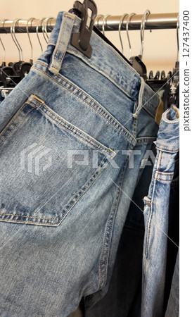 A woman's hand runs over the jeans that hang on hangers in the store. 127437400