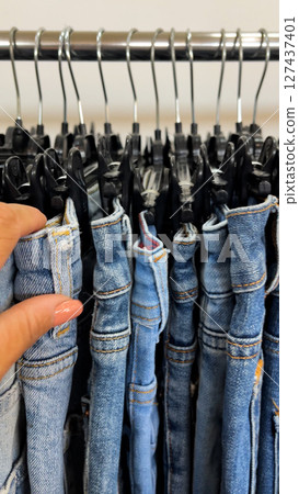 A woman's hand sorts through jeans that hang on hangers in a clothing store. A woman's hand sorts through jeans that hang on hangers in a clothing store. 127437401
