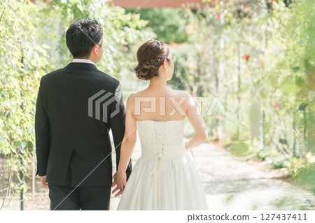 一對穿著禮服的情侶手牽手沿著公園的綠樹成蔭的大道散步(婚禮、婚紗照、新娘和新郎) 一對穿著禮服的情侶手牽手沿著公園的綠樹成蔭的大道散步(婚禮、婚紗照、新娘和新郎) 127437411