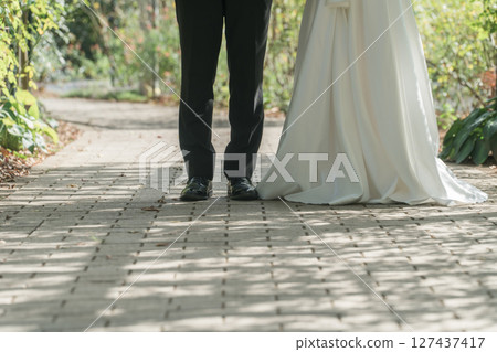 The feet of a couple in dresses walking along a tree-lined path in a park (wedding, wedding photo, bride and groom) 127437417