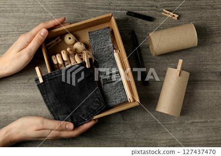 Pieces of denim fabric, paper rolls and box in hands on wooden background, top view Pieces of denim fabric, paper rolls and box in hands on wooden background, top view 127437470