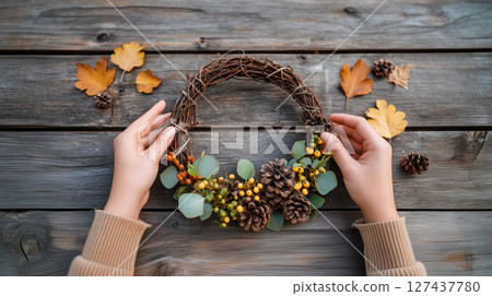 Hands crafting autumn wreath with natural fall decorations Hands crafting autumn wreath with natural fall decorations 127437780