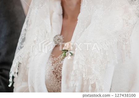 Close-up of a bride s lace jacket adorned with a brooch and a blush peach rose, showcasing intricate detailing and elegant wedding attire. Close-up of a bride s lace jacket adorned with a brooch and a blush peach rose, showcasing intricate detailing and elegant wedding attire. 127438100