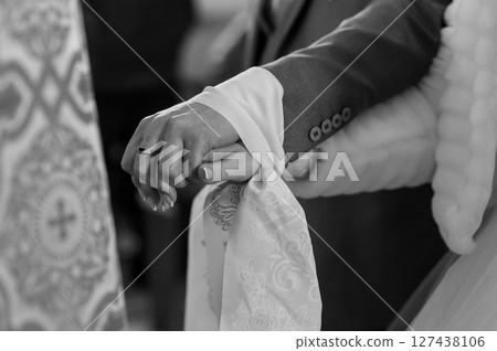 Close-up of hands clasped during wedding ceremony, showing rings and traditional dress details, grayscale photography. Close-up of hands clasped during wedding ceremony, showing rings and traditional dress details, grayscale photography. 127438106