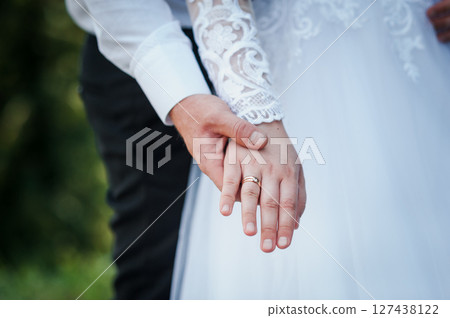 Close-up shot of a wedding couple holding hands with wedding rings visible, symbolizing love, commitment, and marriage outdoors. Close-up shot of a wedding couple holding hands with wedding rings visible, symbolizing love, commitment, and marriage outdoors. 127438122