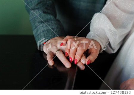 Wedding Rings Close-Up: Hands Holding Together with Red Manicured Nails, Symbolizing Love, Commitment, and a Formal Celebration Wedding Rings Close-Up: Hands Holding Together with Red Manicured Nails, Symbolizing Love, Commitment, and a Formal Celebration 127438123