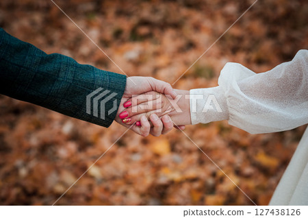 Autumnal Connection: Hands Clasped in a Forest, Love, Relationship, Warmth, and Partnership Represented Through Clothing and Red Nail Polish 127438126