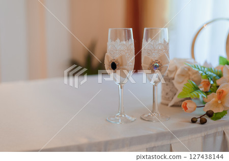 Wedding toasting flutes adorned with delicate lace and sparkling jewel accents, presented on a white tablecloth, symbolizing love and celebration. Wedding toasting flutes adorned with delicate lace and sparkling jewel accents, presented on a white tablecloth, symbolizing love and celebration. 127438144