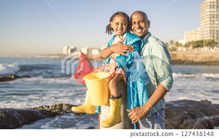 Father, child and family fishing trip at sea learning about nature and having fun on vacation in summer. Portrait of man and girl together teaching kid about fish with beach bucket and net at ocean 127438148