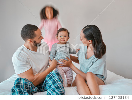 Family, baby and girl jump on bed in bedroom, having fun or playing. Support, love and care of happy father, mother and children bonding, smiling and enjoying quality time together in family house. 127438184