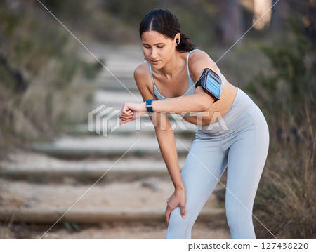 Fitness, running and woman with a smartwatch doing a cardio workout in the woods for health. Sports, wellness and athlete training for a race, marathon or exercise in nature in a forest with a watch. 127438220