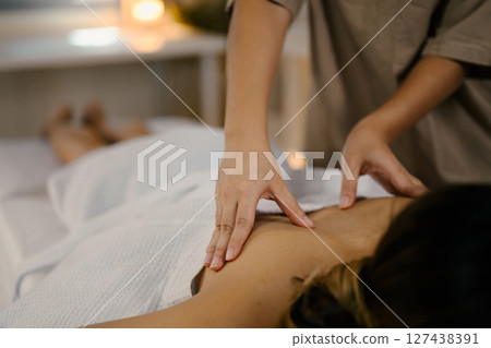 Female client enjoying therapeutic body massage on a treatment table with calm ambiance. Wellness concept 127438391