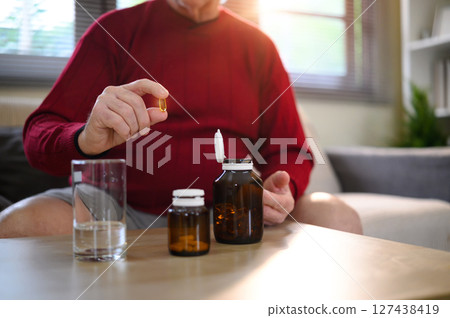 Elderly man preparing to take omega 3 softgel vitamin at home. Health and nutrition concept 127438419