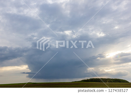 Dark storm clouds gather over a green hillside as the sun sets, signaling an approaching storm Dark storm clouds gather over a green hillside as the sun sets, signaling an approaching storm 127438527
