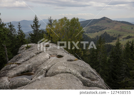 Scenic view from a rocky outcrop overlooking rolling hills and dense forests under a cloudy sky in the mountains Scenic view from a rocky outcrop overlooking rolling hills and dense forests under a cloudy sky in the mountains 127438555