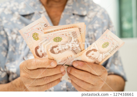 Asian elderly woman holding Thai banknotes money in hand. Poverty, saving problem in retirement. 127438661