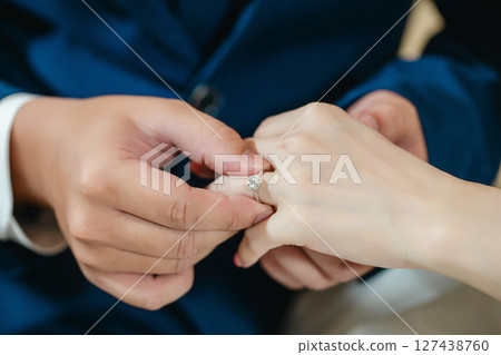 A close-up shot capturing a tender moment as a groom places a sparkling diamond engagement ring on his bride's finger.  127438760