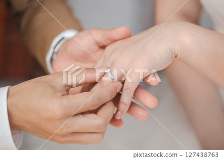 A candid and beautiful shot capturing the pivotal moment during a wedding ceremony where the groom slides the wedding ring onto the bride's finger. 127438763