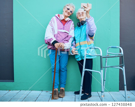 Phone, selfie and disability with senior friends posing for a photograph outdoor on a green wall background. Happy, mobile and walker with a mature woman and friend taking a picture together 127438848
