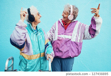 Friends, city and senior women with headphones on blue background wall listening to audio, music and radio. Fashion, style and elderly females enjoy retirement, freedom and dancing in urban town Friends, city and senior women with headphones on blue background wall listening to audio, music and radio. Fashion, style and elderly females enjoy retirement, freedom and dancing in urban town 127438895