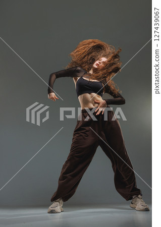 Jazz-funk dancer in fierce motion with flying hair, black outfit, and bold pose on grey studio background. Jazz-funk dancer in fierce motion with flying hair, black outfit, and bold pose on grey studio background. 127439067