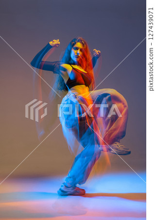 Stylish jazz-funk dancer in motion under vivid studio lighting, with glowing colors and urban dance energy. 127439071