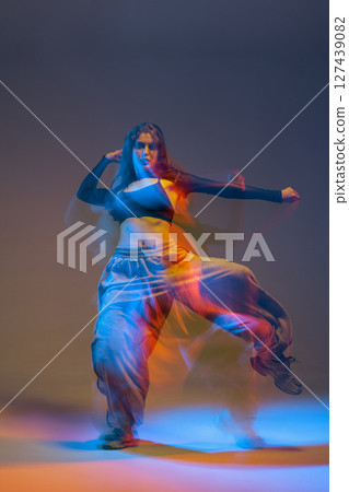 Jazz-funk dancer mid-move with motion blur and neon glow, expressing energy, rhythm, and bold attitude in a creative studio. 127439082