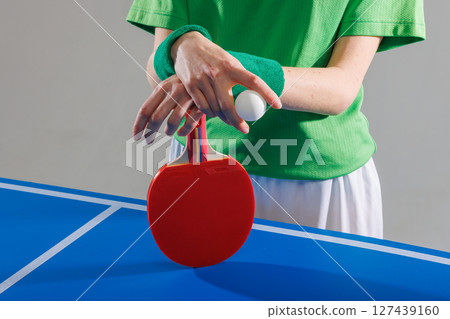 Table tennis player in green preparing to serve, holding ping pong paddle and ball on blue game table. Table tennis player in green preparing to serve, holding ping pong paddle and ball on blue game table. 127439160
