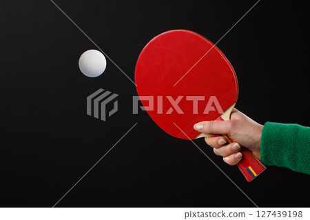 Close-up of red table tennis paddle and white ball in motion against black background, minimal sports concept. 127439198