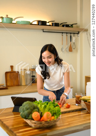 Happy woman slicing tomatoes and cooking healthy meal with online recipe Happy woman slicing tomatoes and cooking healthy meal with online recipe 127440299