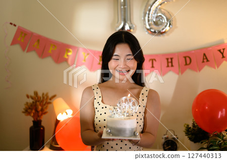 Happy teenage girl holding a birthday cake with candles during a sweet 16 party 127440313