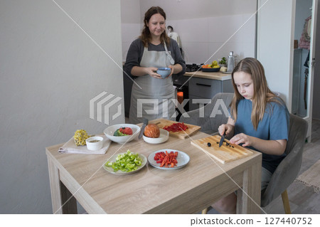 Healthy daughter and her mother cooking in domestic kitchen together, family lifestyle portrait 127440752