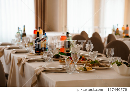 Elegant Wedding Reception Dinner Table Setting with Wine Glasses, Plates, and Floral Decorations in a Luxurious Beige Ballroom. 127440776