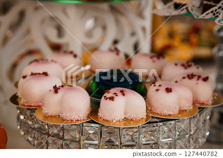 Elegant Pink Rose-Topped Macarons Displayed on Crystal Stand at Luxury Wedding Dessert Table with Sparkling Decorations. 127440782