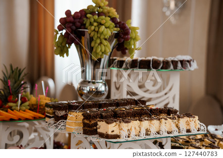 Elegant Dessert Table Arrangement Featuring Chocolate Cake, Grapes, and Fruit Display in a Luxurious Interior Setting, Brown and Beige Tones 127440783