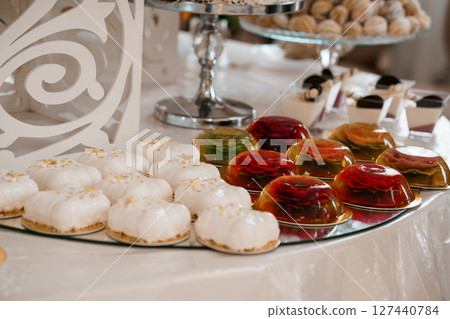 Elegant Wedding Dessert Table Display with White Cakes, Gelatin Cups, and Silverware on a White Linen Setting 127440784