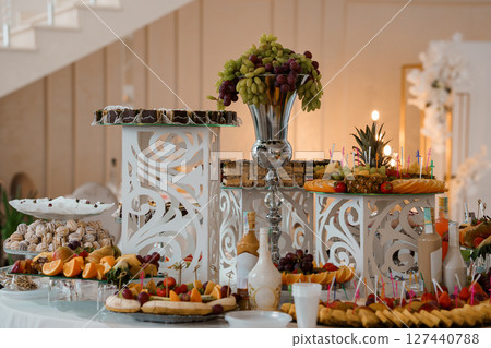 Elegant Wedding Dessert Table with Fruit Abundance. Luxurious Feast Display in Cream and Gold Tone. Celebratory Event Decor Styling Elegant Wedding Dessert Table with Fruit Abundance. Luxurious Feast Display in Cream and Gold Tone. Celebratory Event Decor Styling 127440788