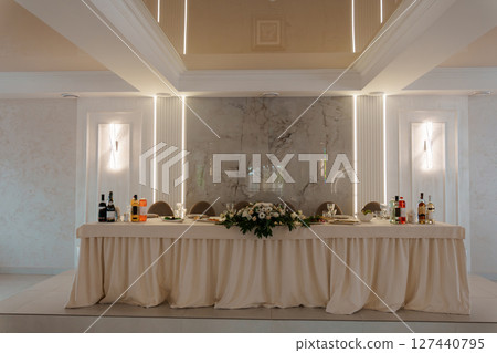 Elegant Wedding Table Setting in Marble Room: Cream Tablecloth, Floral Arrangement, White Columns, Luxurious Interior, Reception Decor, Bridal Celebration Elegant Wedding Table Setting in Marble Room: Cream Tablecloth, Floral Arrangement, White Columns, Luxurious Interior, Reception Decor, Bridal Celebration 127440795